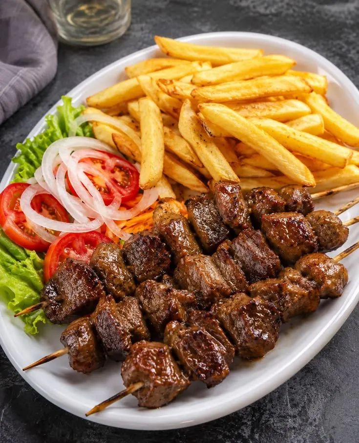 Beef suya skewers plated with chips, onion and fresh salad